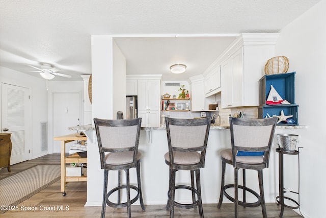 3190 N Atlantic Ave Unit 220, Cocoa Beach, FL 32931 - kitchen featuring white cabinetry, a breakfast bar area, wood finished floors, ceiling fan, and a textured ceiling