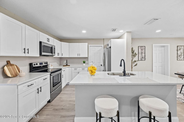 532 Buckingham Ave, Melbourne, FL 32935 - kitchen with stainless steel appliances, a breakfast bar area, white cabinetry, light wood-style flooring, and recessed lighting