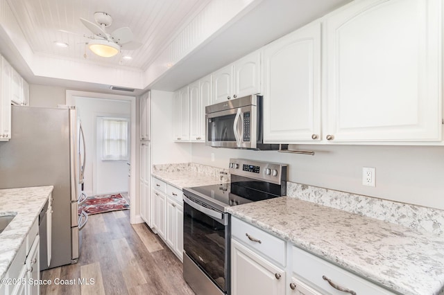 658 Hibiscus Dr, Satellite Beach, FL 32937 - kitchen featuring stainless steel appliances, light wood finished floors, white cabinetry, a tray ceiling, and recessed lighting