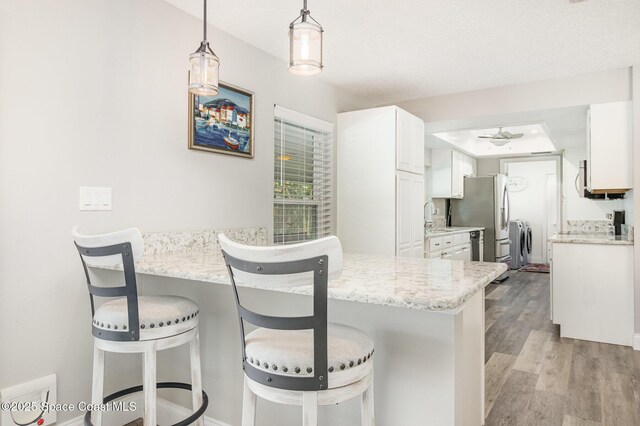 658 Hibiscus Dr, Satellite Beach, FL 32937 - kitchen featuring stainless steel fridge with ice dispenser, white cabinetry, light wood finished floors, and a kitchen breakfast bar