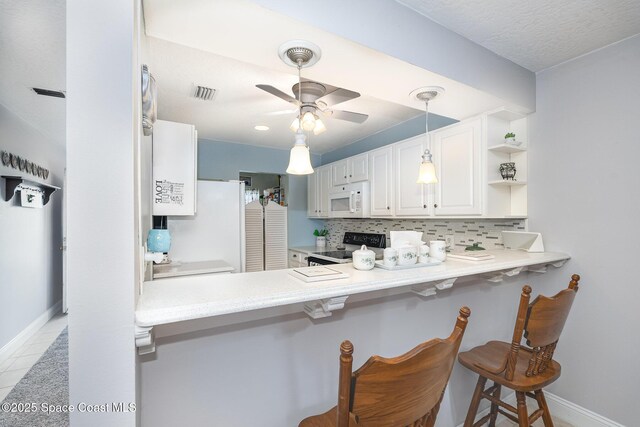 1005 Knox Mcrae Dr Unit B-210, Titusville, FL 32780 - kitchen with white microwave, electric range, tasteful backsplash, ceiling fan, and a breakfast bar area