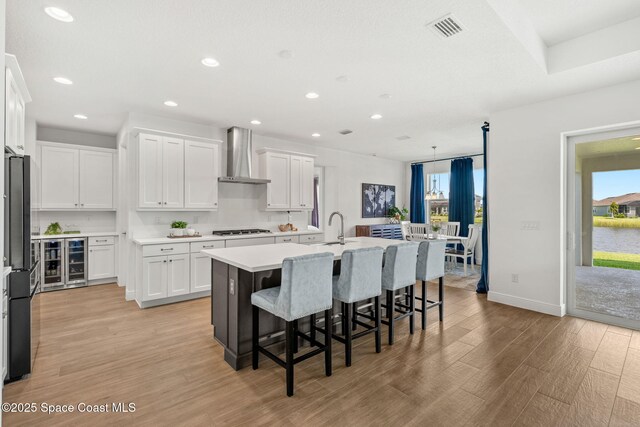 9374 Corvo Ct, Melbourne, FL 32940 - kitchen featuring wall chimney exhaust hood, gas cooktop, light wood-style flooring, freestanding refrigerator, and an island with sink