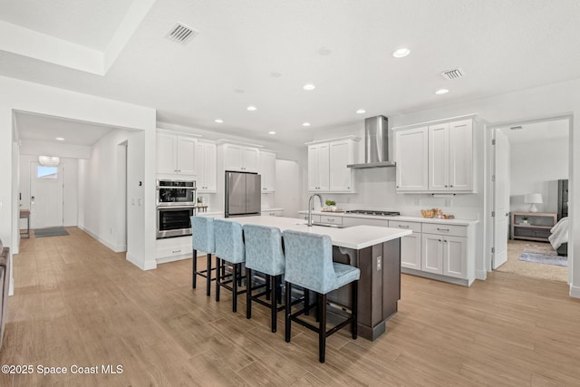 9374 Corvo Ct, Melbourne, FL 32940 - kitchen featuring wall chimney exhaust hood, stainless steel appliances, a breakfast bar area, white cabinets, and a center island with sink