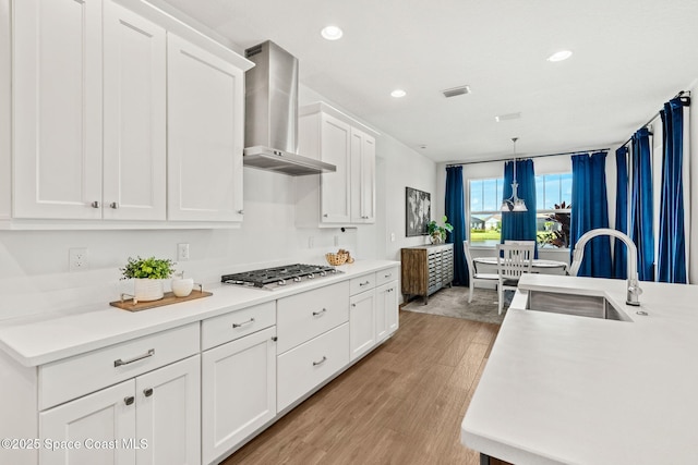 9374 Corvo Ct, Melbourne, FL 32940 - kitchen with wall chimney exhaust hood, stainless steel gas cooktop, light wood-type flooring, white cabinetry, and light countertops