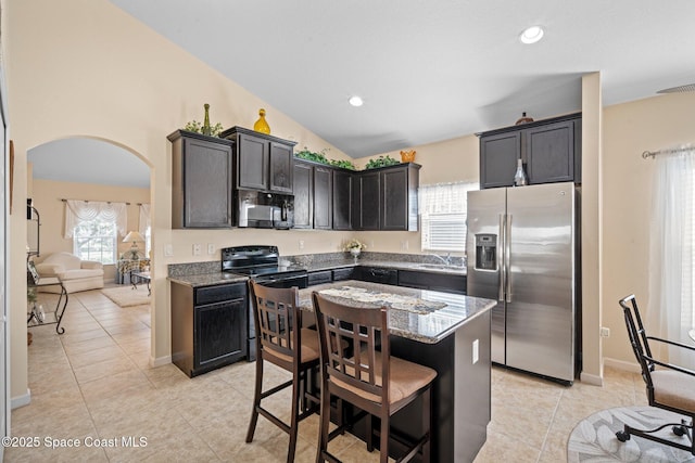 103 Amherst Ln, Sebastian, FL 32958 - kitchen featuring black appliances, arched walkways, dark stone counters, light tile patterned flooring, and vaulted ceiling