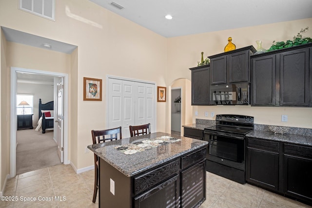 103 Amherst Ln, Sebastian, FL 32958 - kitchen featuring black appliances, dark cabinets, arched walkways, dark stone countertops, and a kitchen island