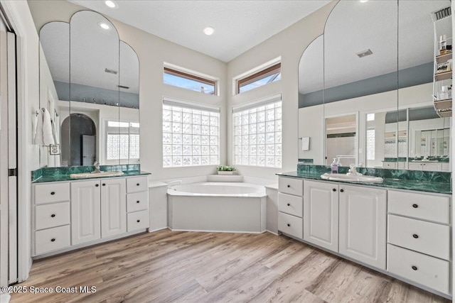 442 Carmel Dr, Melbourne, FL 32940 - bathroom featuring wood finished floors, a garden tub, two vanities, and recessed lighting