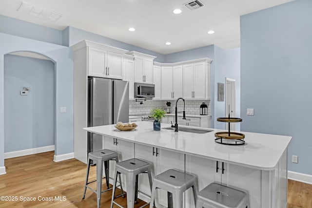 2559 Christopher Dr, Titusville, FL 32780 - kitchen featuring stainless steel appliances, white cabinetry, backsplash, a kitchen breakfast bar, and light wood-style floors