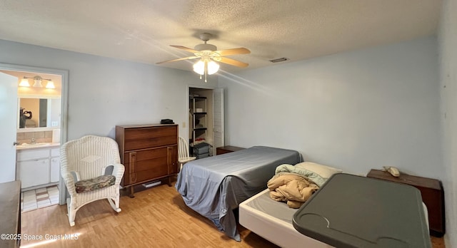 1469 California Dr, Melbourne, FL 32940 - bedroom with light wood-style floors, a textured ceiling, connected bathroom, and a ceiling fan