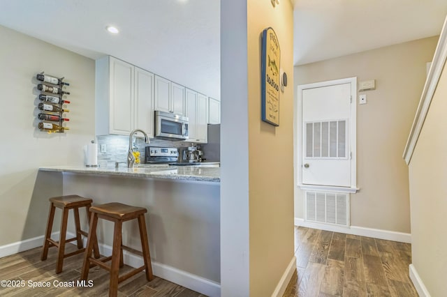 57 Broad St Unit 6, Titusville, FL 32796 - kitchen featuring stainless steel appliances, dark wood-style flooring, white cabinetry, a kitchen breakfast bar, and light stone counters
