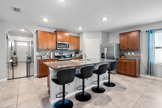820 Old Country Rd SE, Palm Bay, FL 32909 - kitchen with stainless steel appliances, brown cabinetry, decorative backsplash, light tile patterned floors, and dark stone countertops
