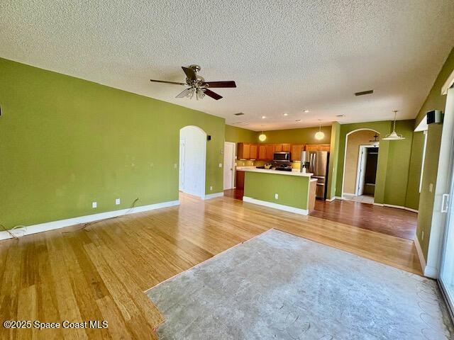 968 Shaw Cir, Melbourne, FL 32940 - unfurnished living room with arched walkways, light wood-style floors, a ceiling fan, and a textured ceiling