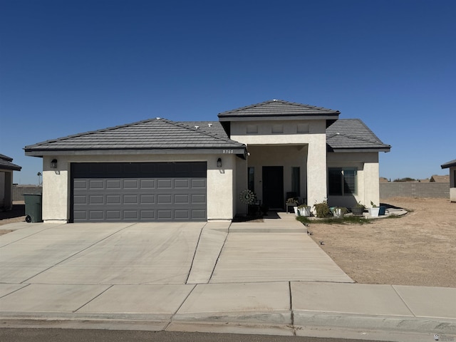 prairie-style house with a garage, driveway, a tiled roof, and stucco siding