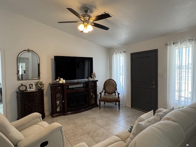 living area featuring ceiling fan, light tile patterned floors, a textured ceiling, a fireplace, and vaulted ceiling