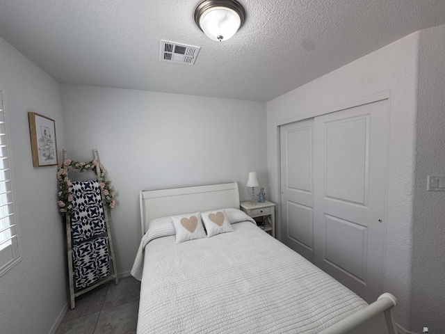 bedroom featuring baseboards, visible vents, tile patterned flooring, a textured ceiling, and a closet