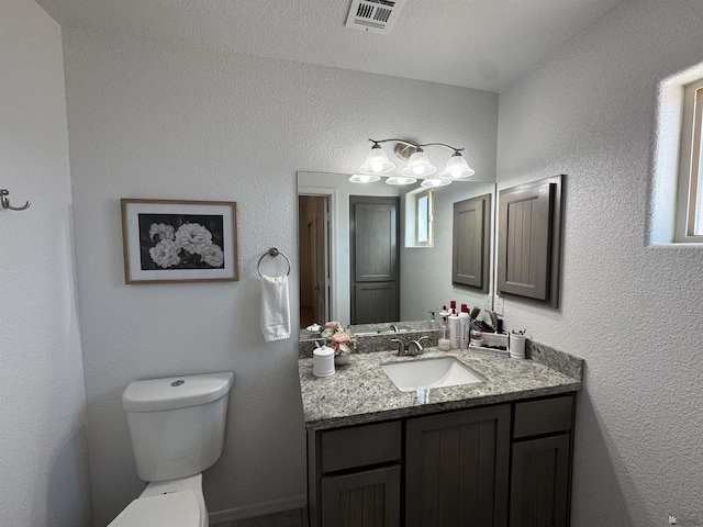 bathroom featuring toilet, a textured wall, visible vents, and vanity