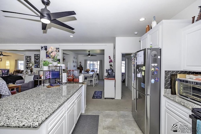 kitchen featuring open floor plan, light stone counters, freestanding refrigerator, and white cabinetry