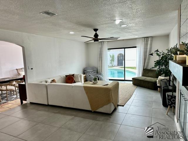 living room featuring ceiling fan, light tile patterned floors, and a textured ceiling