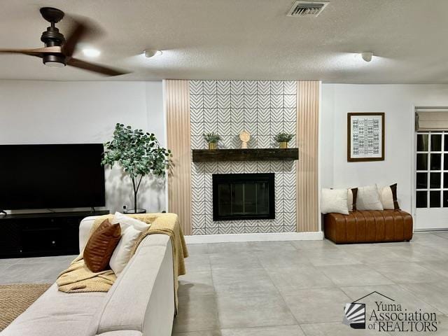 living room with ceiling fan, a textured ceiling, and a fireplace