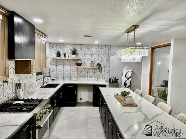 kitchen with sink, high end stainless steel range oven, hanging light fixtures, light stone countertops, and a textured ceiling