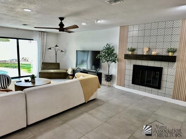 living room with ceiling fan, a fireplace, and a textured ceiling