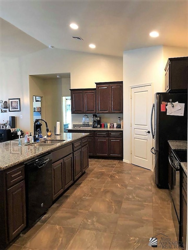 kitchen with vaulted ceiling, black appliances, sink, light stone counters, and dark brown cabinetry