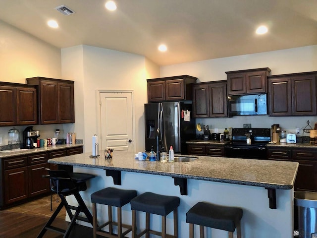 kitchen with dark brown cabinetry, a breakfast bar, a center island with sink, and black appliances