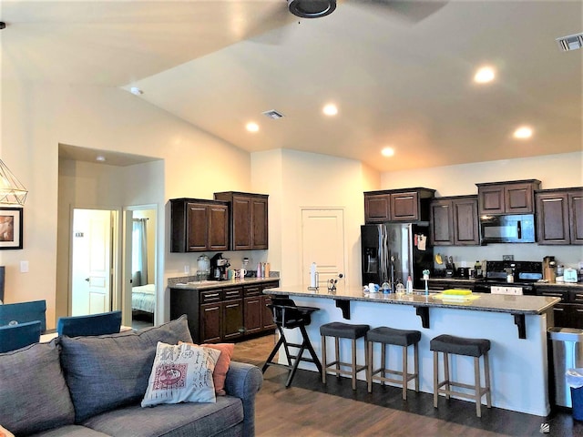 kitchen featuring a kitchen breakfast bar, dark brown cabinetry, black appliances, an island with sink, and dark hardwood / wood-style flooring