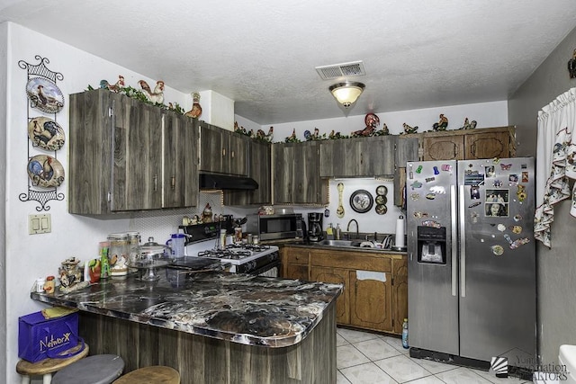 kitchen featuring appliances with stainless steel finishes, sink, light tile patterned floors, dark brown cabinetry, and a textured ceiling