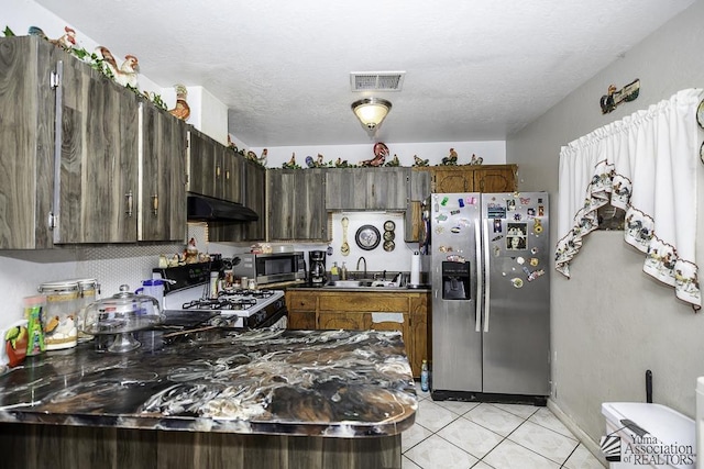 kitchen with appliances with stainless steel finishes, sink, light tile patterned floors, dark brown cabinets, and a textured ceiling