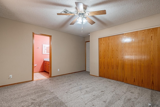 unfurnished bedroom with ceiling fan, ensuite bathroom, light colored carpet, a textured ceiling, and a closet