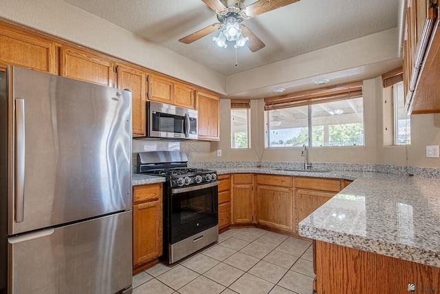 kitchen with ceiling fan, sink, light stone counters, light tile patterned floors, and appliances with stainless steel finishes