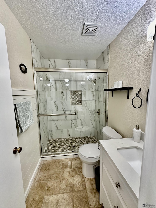 bathroom featuring visible vents, a textured wall, toilet, a shower stall, and a textured ceiling