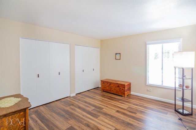 bedroom featuring two closets, baseboards, and wood finished floors