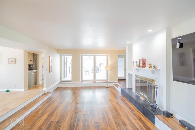 unfurnished living room featuring light wood-style floors, a tile fireplace, baseboards, and recessed lighting