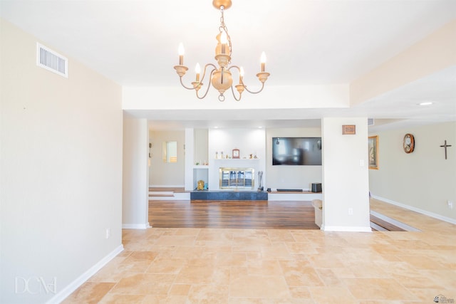 unfurnished living room featuring a chandelier, a glass covered fireplace, visible vents, and baseboards