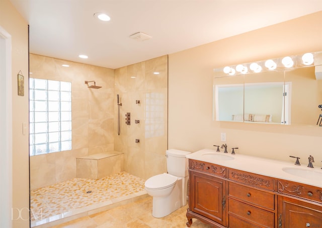 full bathroom with toilet, double vanity, a tile shower, and a sink