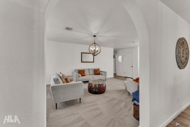 living room featuring baseboards, visible vents, arched walkways, a textured wall, and a chandelier