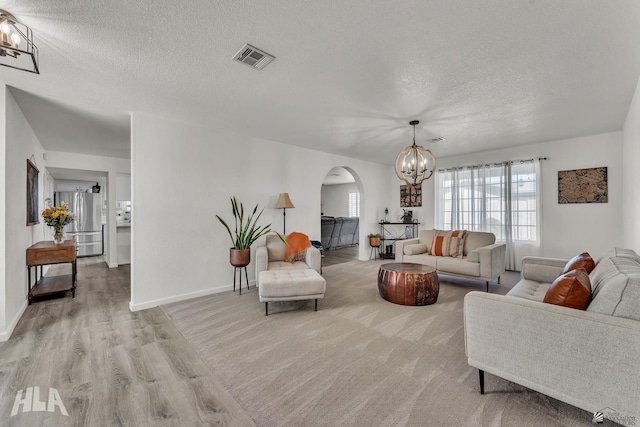 living area with arched walkways, a notable chandelier, visible vents, light wood-style flooring, and a textured ceiling