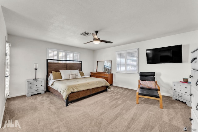 bedroom with baseboards, visible vents, light colored carpet, ceiling fan, and a textured ceiling