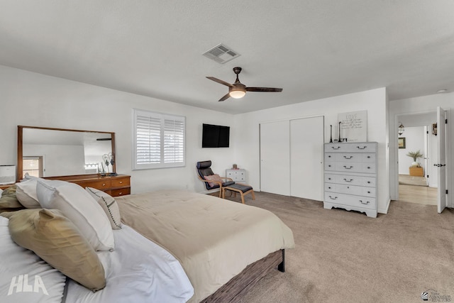 bedroom with a closet, visible vents, light carpet, ceiling fan, and a textured ceiling