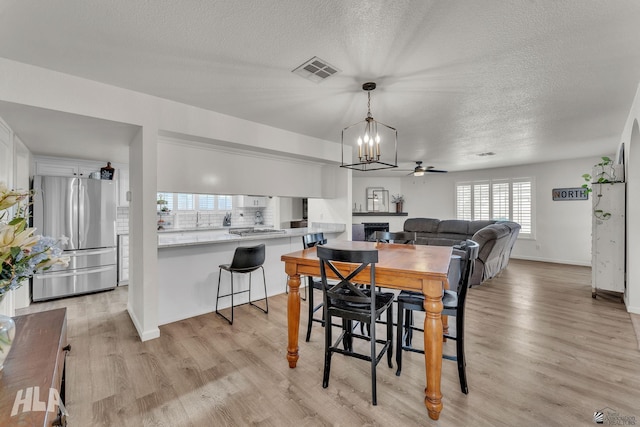 dining space featuring a textured ceiling, ceiling fan, visible vents, baseboards, and light wood-style floors