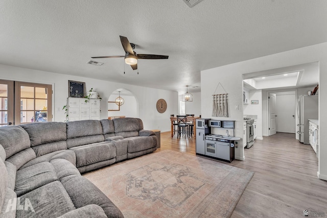 living room with light wood-type flooring, a textured ceiling, a ceiling fan, and french doors