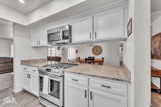 kitchen with stainless steel appliances, light wood-style floors, a healthy amount of sunlight, white cabinets, and light stone countertops