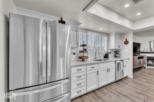 kitchen with appliances with stainless steel finishes, light wood-style floors, white cabinets, and a sink