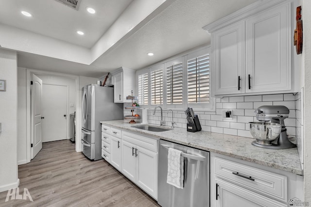 kitchen featuring stainless steel appliances, tasteful backsplash, light wood-style flooring, white cabinetry, and a sink