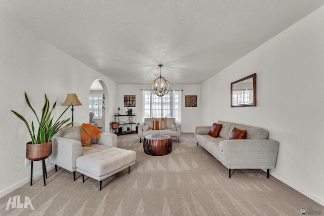 living area featuring arched walkways, light carpet, a textured ceiling, and baseboards