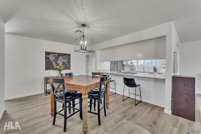 dining room with a chandelier, baseboards, a textured ceiling, and light wood finished floors