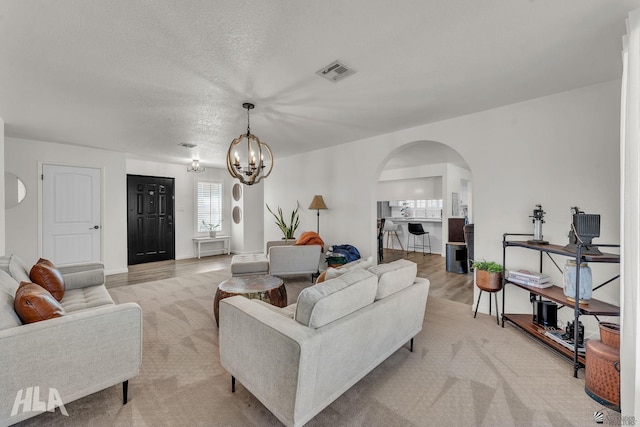 living area featuring arched walkways, a textured ceiling, light wood-style flooring, visible vents, and an inviting chandelier