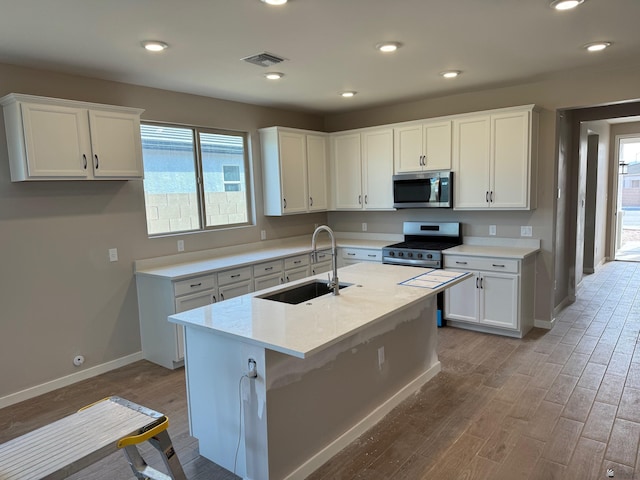 kitchen with appliances with stainless steel finishes, a wealth of natural light, sink, white cabinets, and a kitchen island with sink